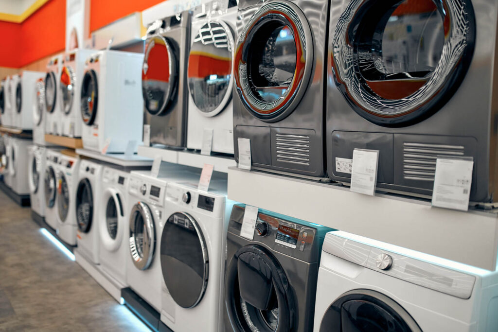 An assortment of beautiful stylish washing machines on showcases in a gadget, electronics and household appliances store.